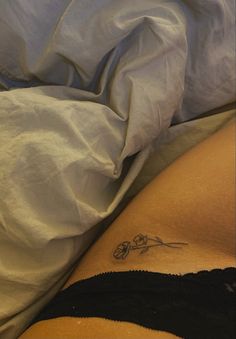 a woman laying in bed with a tattoo on her lower back and stomach, under a blanket