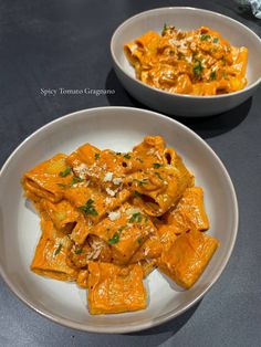 two white bowls filled with pasta and sauce on top of a black countertop next to each other