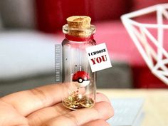 a person holding a tiny glass bottle with a pokeball in it that says i choose you