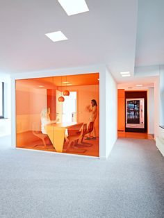 an office with orange glass walls and people sitting at a table in the middle of the room