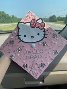 a pink hello kitty graduation cap sitting on the dashboard of a car with silver sequins