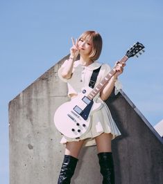 a woman in short white dress holding a guitar and posing with her hand up to her face