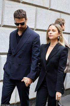 a man and woman are walking down the street holding hands while wearing black suits with sunglasses on their heads