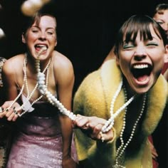 two women with pearls on their neck and necklaces in front of them, laughing