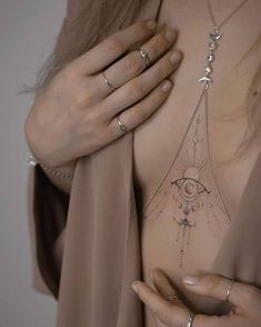 a woman's chest with an all seeing eye tattoo on her left shoulder and two rings around her neck