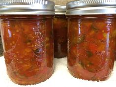 two jars filled with pickled vegetables sitting on top of a white cloth covered table