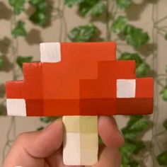 a hand holding up a piece of paper that looks like a mushroom with red and white squares on it