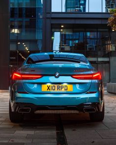 the rear end of a blue bmw car parked in front of a large glass building