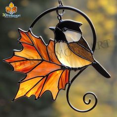 a stained glass bird sitting on top of an orange leaf hanging from a metal hook