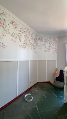 a woman sitting on the floor in front of a wall with flowers painted on it