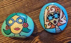 two painted rocks sitting on top of a wooden table next to each other, one with a woman's face