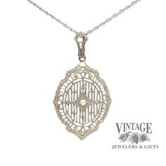 The detail of this antique vintage 14 karat white gold filigree pendant is noteworthy as it offers a shield shape with filigree spokes from top to bottom in a linear design. The filigree is joined by 6 small fleur-des-lis and 2 floral designs. The .02 carat single cut SI quality diamond is illusion set in a small diamond shape inset in the center of the pendant while the scallopped and reeded edge gives it even more character. The pendant is suspended from a milgrain etched bale on a 18" fine op Antique White Gold Necklace With Diamond Accents, Classic Sterling Silver Diamond Necklace With Oval Pendant, Art Deco White Gold Oval Necklace, Antique White Gold Filigree Necklace, Antique Silver Diamond Necklace With Diamond Accents, Vintage White Gold Necklace With Diamond Accents, Antique White Gold Necklace With Filigree, Antique White Gold Necklace With Intricate Design, Formal White Gold Filigree Jewelry