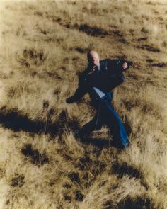 a man is sitting in the middle of an open field with his head on his back