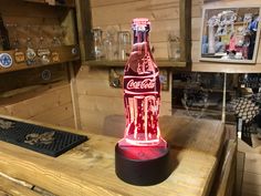 a coca - cola bottle shaped lamp sitting on top of a wooden table in a store