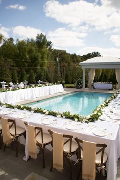 a long table set up with white linens next to a swimming pool