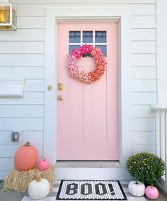 a pink front door with a wreath and pumpkins