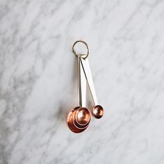 two metal spoons sitting next to each other on a marble counter top with a pair of tongs hanging from it