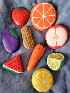 painted rocks with fruits and vegetables on them sitting on a blue cloth covered tablecloth