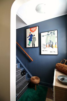 two pictures hang on the wall next to a stair case in a room with blue walls and green carpet