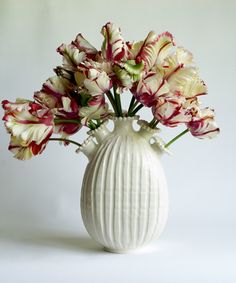 a white vase with red and white flowers in it on a white tablecloth background