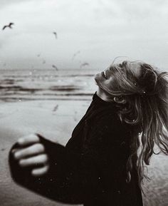 a black and white photo of a woman on the beach with seagulls in the background