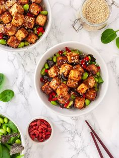 two bowls filled with tofu and vegetables next to chopsticks on a table