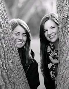 two young women are peeking out from behind the trees, posing for a black and white photo