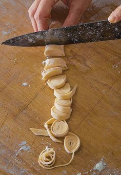 a person holding a knife over some food on a cutting board with pasta spirals