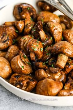 a white bowl filled with cooked mushrooms and garnished with parsley