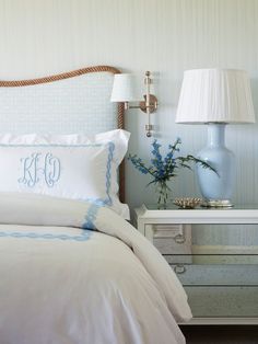 a bed with white sheets and blue pillows in a bedroom next to a lamp on a nightstand