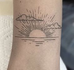 a small sun and clouds tattoo on the left arm with black ink above it, in front of a white background