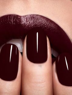 a woman's hands with dark colored nails and maroon lipstick