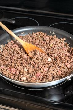 a skillet filled with ground beef cooking on top of an electric stove next to a wooden spatula