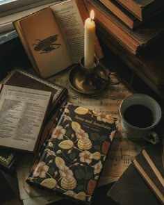 an open book, cup of coffee and some books on a table with a candle