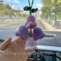 a hand holding three crocheted flowers in front of a car dashboard with the steering wheel behind it