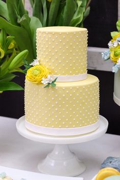 a three tiered yellow cake with white polka dots and flowers on the top layer