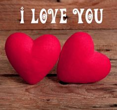 two red hearts sitting next to each other on top of a wooden table with the words i love you