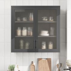 a kitchen cabinet with glass doors and wooden cutting board on the counter top next to utensils