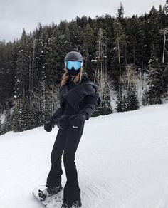 a person on a snowboard is standing in the snow with trees behind them and wearing goggles