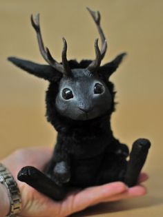 a hand holding a tiny black animal with horns