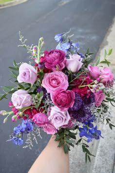 a person holding a bouquet of flowers in their hand on the street with cars behind them