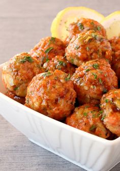 a white bowl filled with meatballs covered in sauce and garnished with lemon wedges