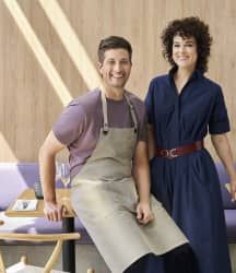 a man and woman standing next to each other in front of a table with chairs