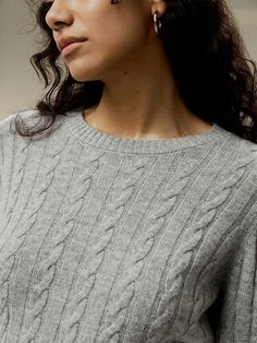 a woman in grey sweater and earrings looking off to the side with her hand on her hip