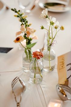 two vases with flowers are sitting on a table next to forks and spoons