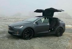 an electric car with its doors open sitting in the middle of a gravel road on a foggy day