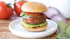 a hamburger with lettuce, tomato and onion on a plate next to tomatoes