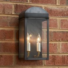 two lit candles are attached to the side of a brick wall mounted light fixture,