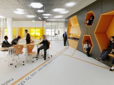 an office with people sitting at desks and standing in front of orange cubicles