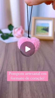 someone is holding a pink ball on a string with the caption pompom artesanal em formato de coraco